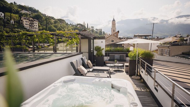 Una terraza en la azotea con jacuzzi, mobiliario exterior y vistas a una montaña y una iglesia.