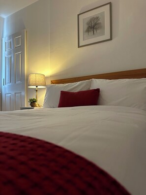 Cozy retreat with a neatly made bed, framed artwork, and a table lamp.