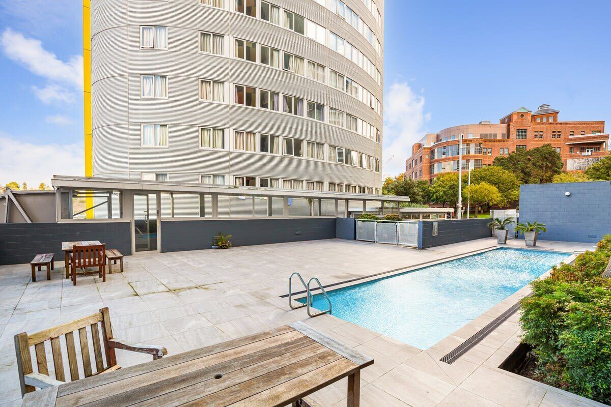 A modern building with a pool, outdoor seating, and a clear sky.