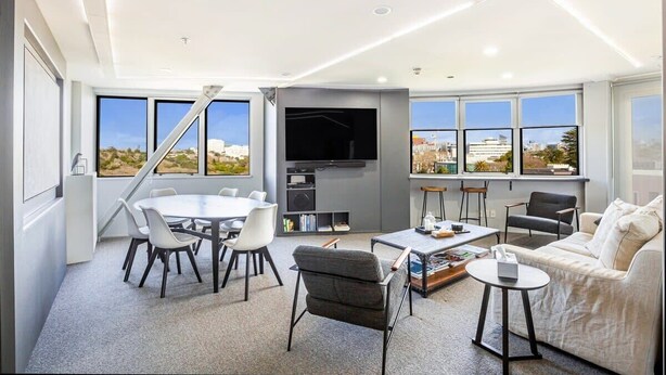 A modern living room with a dining area, a sofa, a TV, and large windows with a city view.