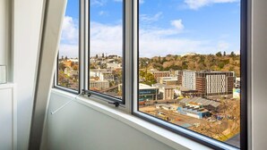 A room with a large window overlooking a cityscape with modern buildings and a hill in the distance.