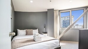 A modern hotel room with a large bed, a desk, and a window with a city view.