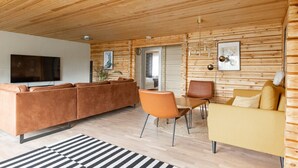 Een moderne woonkamer met een houten plafond, een bank, een gele zitzak, een televisie en een eethoek met stoelen.