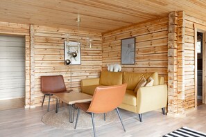 A log cabin interior with a wooden wall, a sofa, a table, and two chairs. - Cozy lodge surrounded by lake (Petäjävesi)