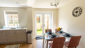 Une cuisine moderne avec un coin repas, une horloge au mur et une vue à travers la porte vitrée.