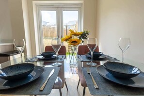 Une table à manger dressée pour quatre personnes, avec des assiettes noires, des couverts en argent et des verres à vin, et un vase rempli de tournesols placé au centre.