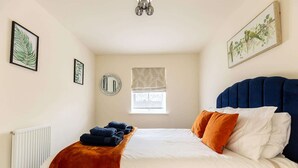 Une chambre à coucher avec un lit, une fenêtre avec des stores, un miroir et des œuvres d’art accrochées aux murs.