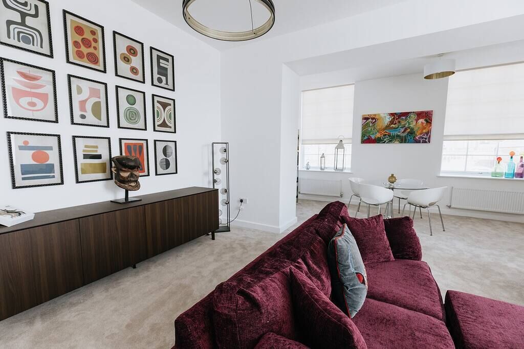 Un salon moderne avec une console de couleur marron foncé, un canapé en velours rouge et un coin repas comprenant une table et des chaises blanches.