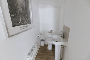 A small, white bathroom with a framed photograph of a street scene, a toilet, and a sink. - Grade II mill townhouse Leeds | Parking | Sleeps 6 (Leeds)
