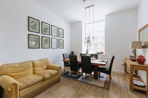 A modern living room with a yellow sofa, a dining table with chairs, and framed botanical prints on the wall. - Grade II mill townhouse Leeds | Parking | Sleeps 6 (Leeds)