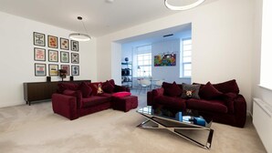 Ein modernes Wohnzimmer mit zwei roten Sofas, einem Glastisch und einem Essbereich, der durch eine offene Tür erkennbar ist.