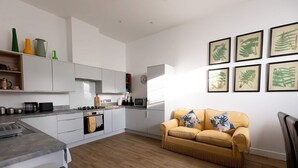 Eine moderne Küche mit weißen Schränken, einem gelben Sofa und gerahmten Pflanzenbildern an der Wand.