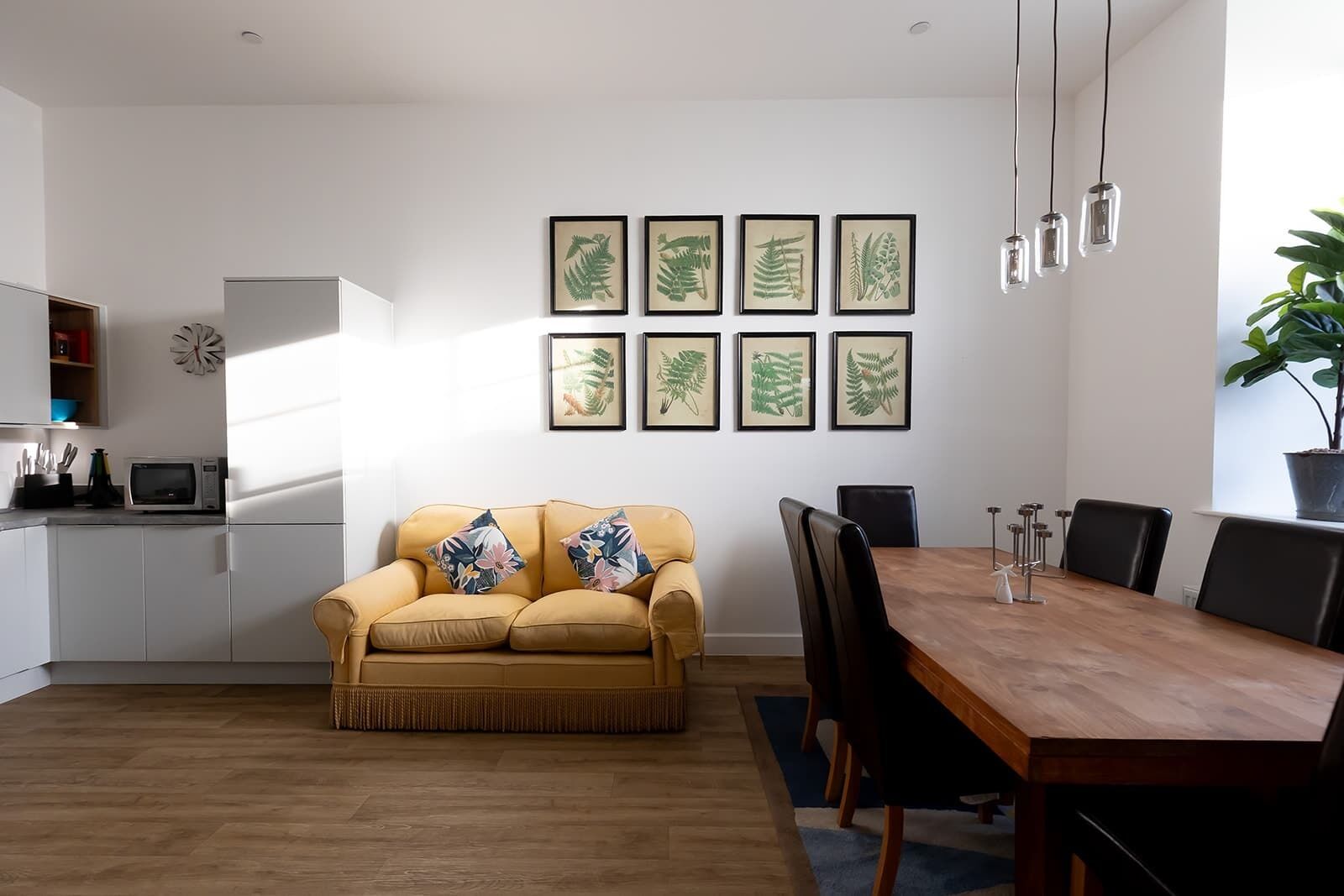 A modern living room with a sofa, dining table, chairs, and framed botanical prints on the wall.