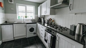 A compact kitchen with white cabinets, a washing machine, a stove, and a kettle. - 4 Bed Property on the Edge of the National Park (Derbyshire)