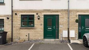 A row of townhouses with a central green door, a small outdoor trash bin, and a parked car. - 4 Bed Property on the Edge of the National Park (Derbyshire)