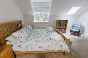 Een slaapkamer met een houten bed, een raam, een boekenplank en een stoel.