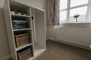 Een kamer met een witte boekenkast, een radiator en een raam met bloemen gordijnen.