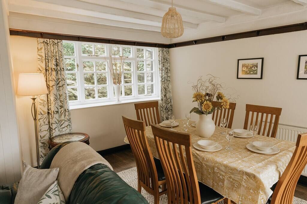 A dining area with a table set for four, surrounded by wooden chairs, a vase of sunflowers, and a lamp on a side table.