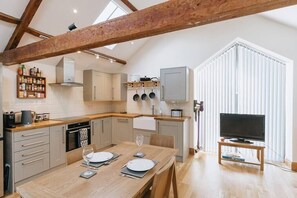 Eine moderne Küche mit Holzbalken, einem für zwei Personen gedecktem Esstisch und einem Fernseher in einer Ecke.