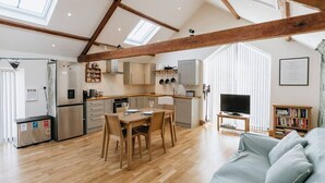 A modern kitchen with wooden beams, a dining area, a living room with a sofa, and a TV. - Converted Barn near Lake District National Park (Carlisle)