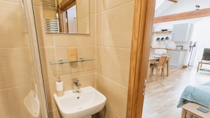 A bathroom with a glass shower enclosure, a white sink, and a wooden door leading to a bedroom. - Converted Barn near Lake District National Park (Carlisle)