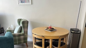 A dining area with a round wooden table, two chairs, a green plaid armchair, and a trash bin. - Perfect Location Near Beach, Shops and Restaurants (Eastbourne)