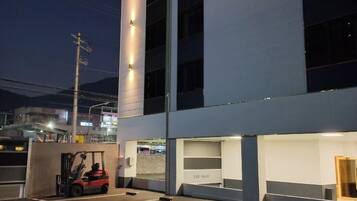 Uma área de estacionamento com um empilhador, um edifício com janelas iluminadas e um céu claro.