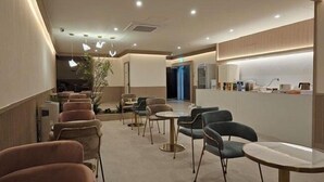 A modern cafe with round tables and chairs, a reception desk, and a plant in the center. - Denbastar Hotel-Kyungnam University Branch (Changwon)