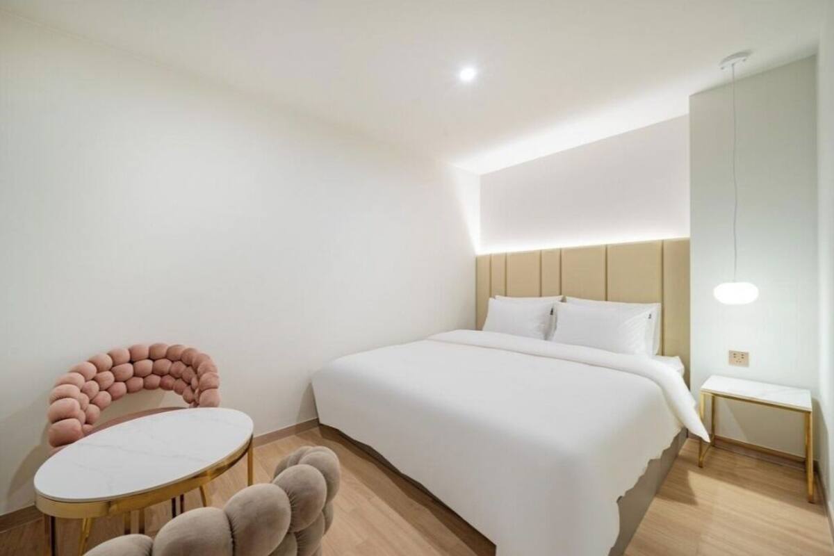 A modern hotel room with a large bed, a round table, and a unique pink chair.
