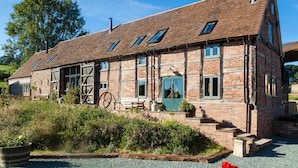 Un bâtiment traditionnel en briques, doté d’un toit en pente, de nombreuses fenêtres et d’une brouette en bois à l’extérieur.