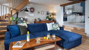 Un salon moderne avec un canapé bleu, une table basse en bois et un escalier menant à la cuisine.