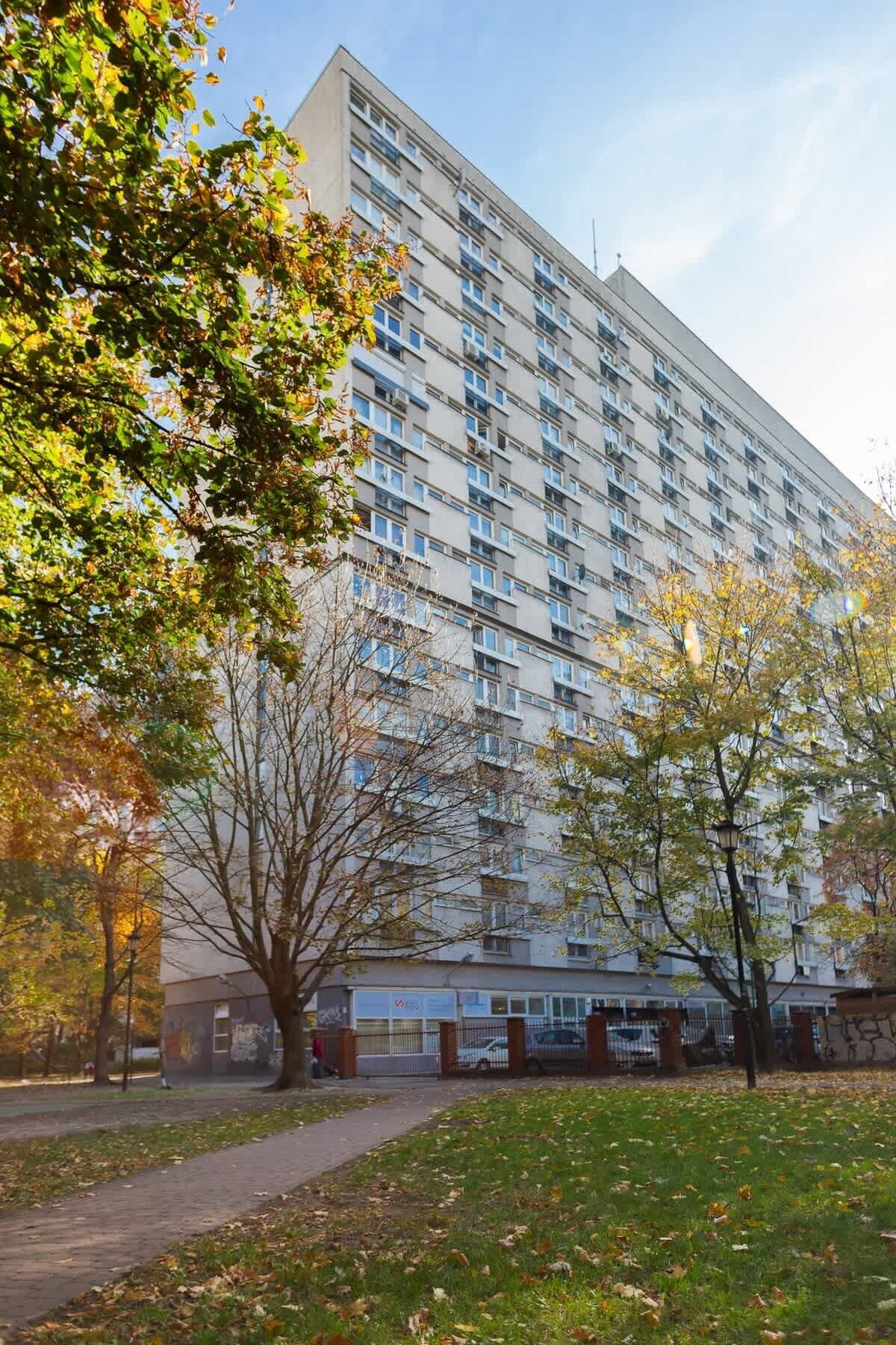 Un immeuble résidentiel à plusieurs étages, doté d’une façade uniforme, entouré d’arbres et d’une zone verdoyante.