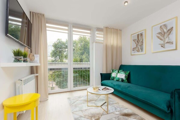 Una sala de estar moderna con un sofá verde, un sillón amarillo, una mesa de centro redonda y un ventanal con vistas a zonas verdes.