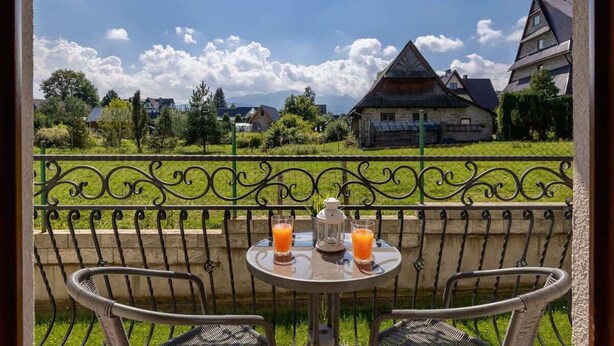 A balcony with a table, two chairs, and two glasses of orange juice.