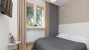 Ein Schlafzimmer mit einem Bett, einem Vorhangfenster, einem kleinen Tisch mit Pflanze und einer Heizung.