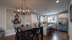 A modern kitchen with white cabinets, a central island, and a dining area with a dark wooden table and chairs. - Private Deck, Views, & Mini-Golf! 10 to Downtown! (Nashville)