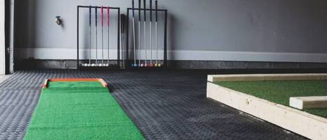 A room with a green carpet, a wooden playpen, and a wall-mounted rack with pool cues.