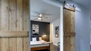 A bedroom with a wooden bed frame, a ceiling fan, and a sliding barn door. - Private Deck, Views, & Mini-Golf! 10 to Downtown! (Nashville)