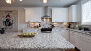 A kitchen with white cabinets, granite countertops, a central island with a bowl of fruit, and a mural of a cowboy on the wall. - Private Deck, Views, & Mini-Golf! 10 to Downtown! (Nashville)