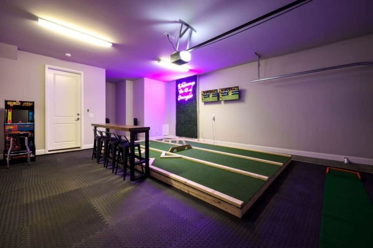 A room with a pool table, bar stools, a neon sign, and a projector on the ceiling.