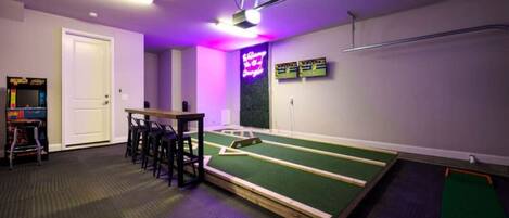 A room with a pool table, bar stools, a neon sign, and a projector on the ceiling.
