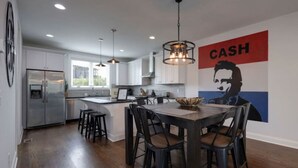 A modern kitchen with white cabinets, a stainless steel refrigerator, pendant lights, and a dining area with a wooden table and black chairs.