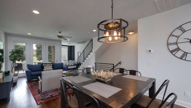 A modern dining area with a wooden table, black chairs, and a large wall clock.