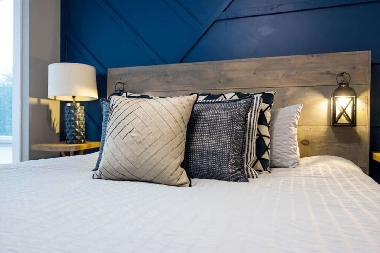 Una cama con almohadas estampadas, cabecera de madera y dos lámparas fijadas a la pared.