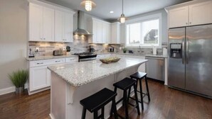 A modern kitchen with white cabinets, granite countertops, a stainless steel refrigerator, and a central island with bar stools.