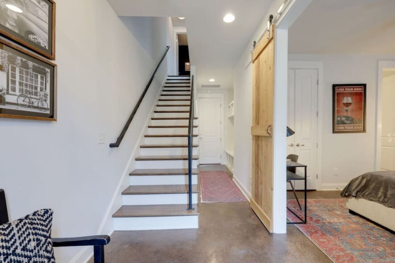 Una escalera que lleva a un dormitorio con una cama, una silla y una puerta.