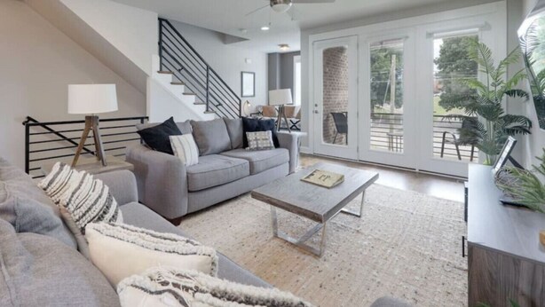 A modern living room with a grey sofa, a coffee table, and a staircase leading to a balcony.