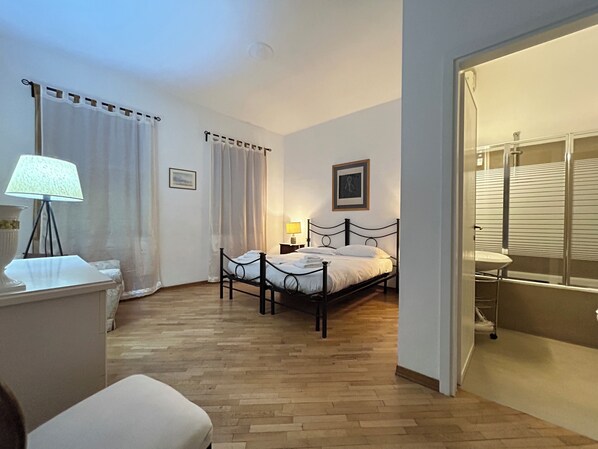 A bedroom with a bed, a bedside table, a lamp, a picture on the wall, and a bathroom visible through an open door.