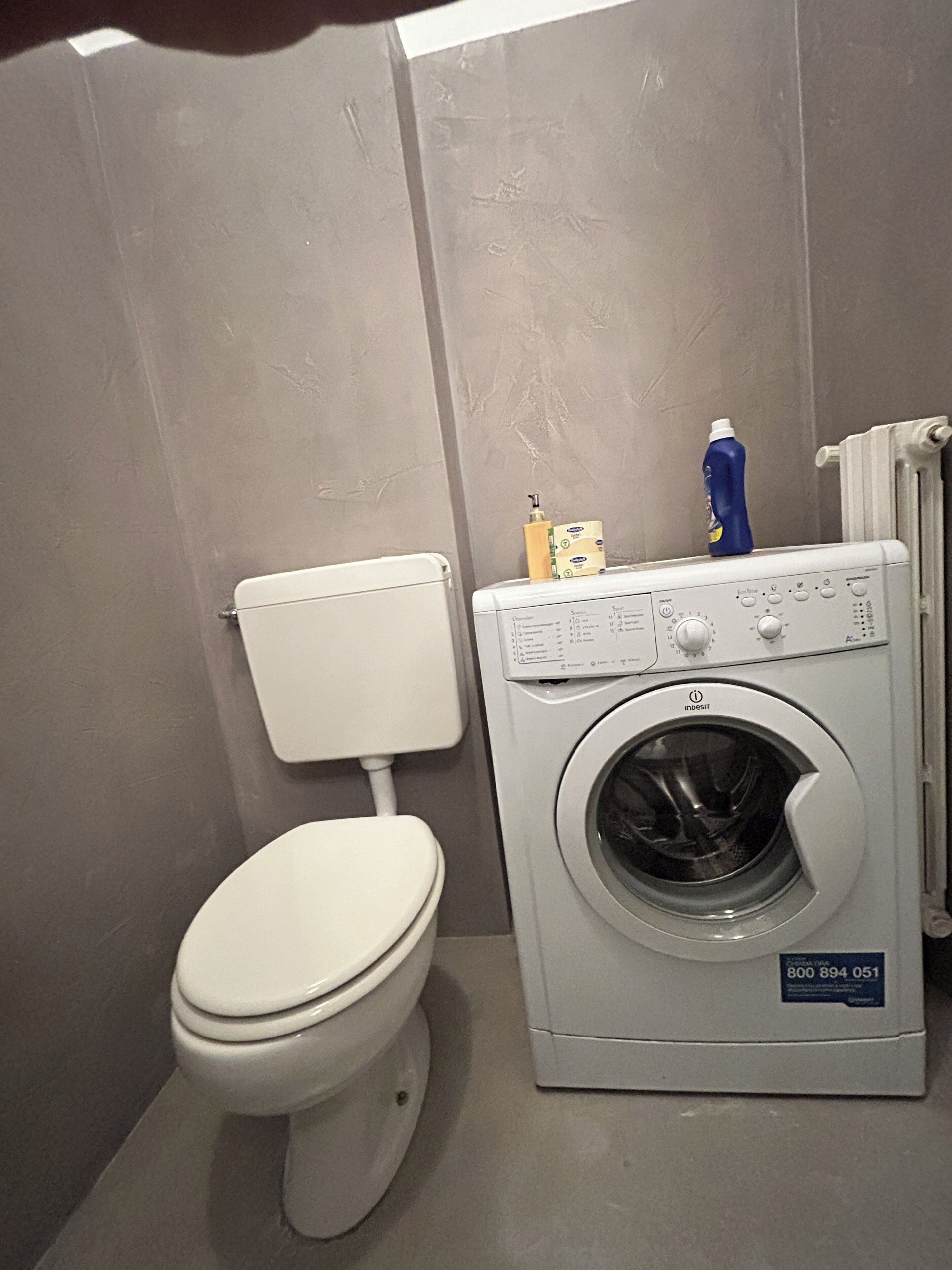 Een kleine badkamer met een wit toilet en een voorlader wasmachine.