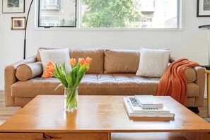 Un salon avec un canapé en cuir marron, un vase en verre contenant des tulipes orange et une table basse en bois sur laquelle sont posés des livres.